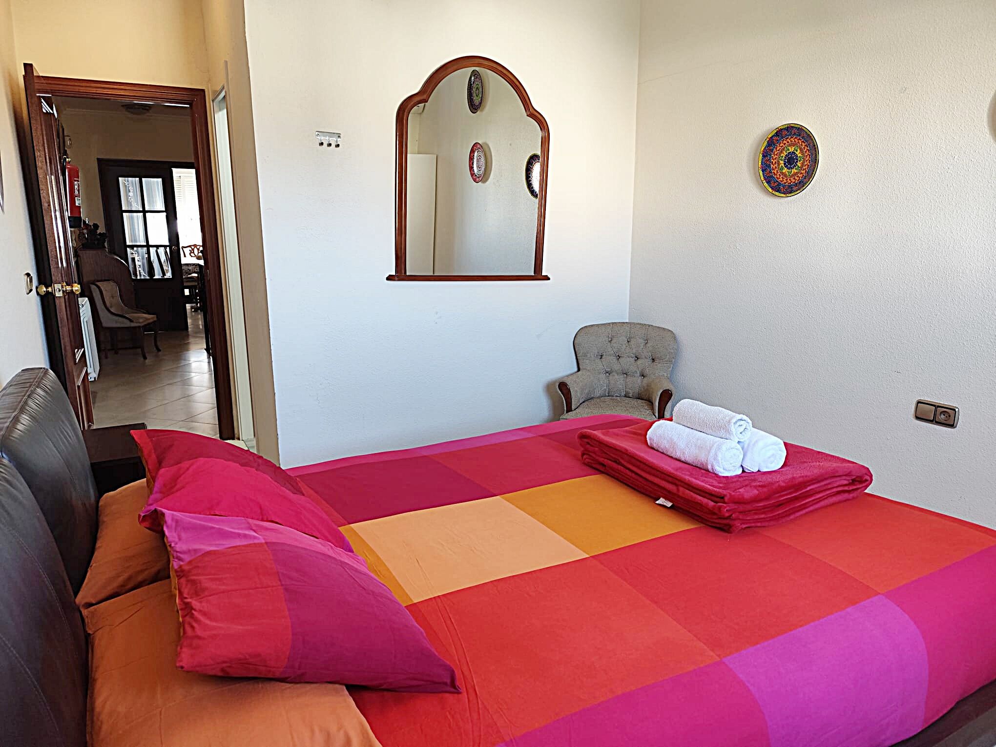 A hotel room with a large bed, a chair, a mirror, and a wall with a decorative plate.