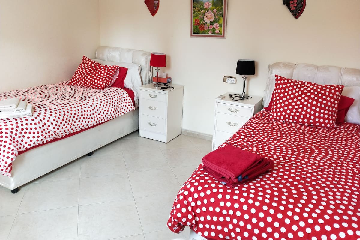 A hotel room with two beds, each with red and white polka dot bedding, white headboards, and matching red pillows. There are two bedside tables with lamps and a small painting on the wall.
