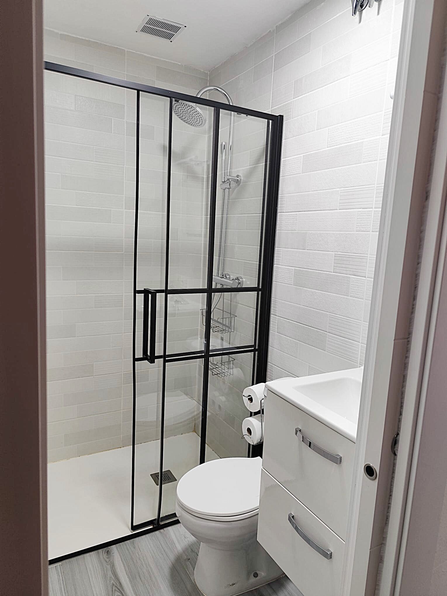 Ein modernes Badezimmer mit einer gläsernen Duschkabine, einer weißen Toilette und einem Stauraumschrank.