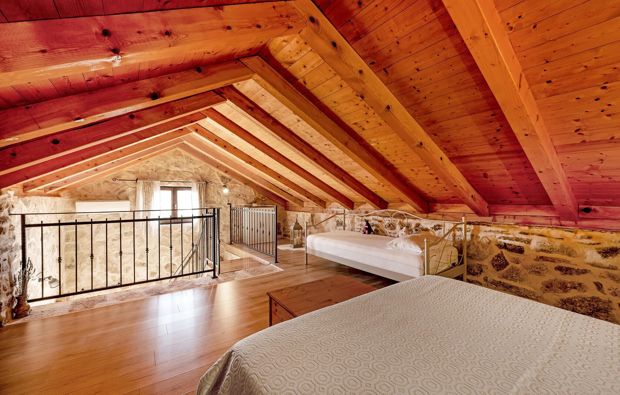 Un dormitorio rústico en el ático con vigas de madera a la vista, una pared de piedra y una cama con colcha estampada.