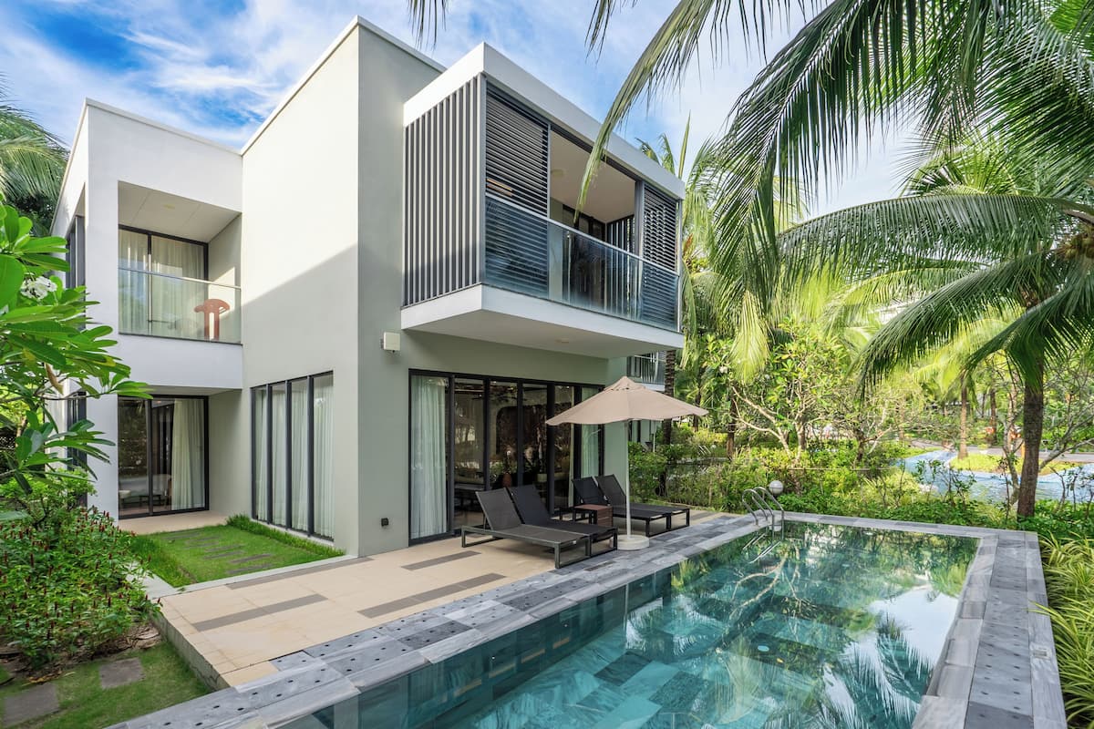Ein modernes, zweistöckiges Haus mit Swimmingpool, Sitzgelegenheiten im Freien und üppiger Bepflanzung.