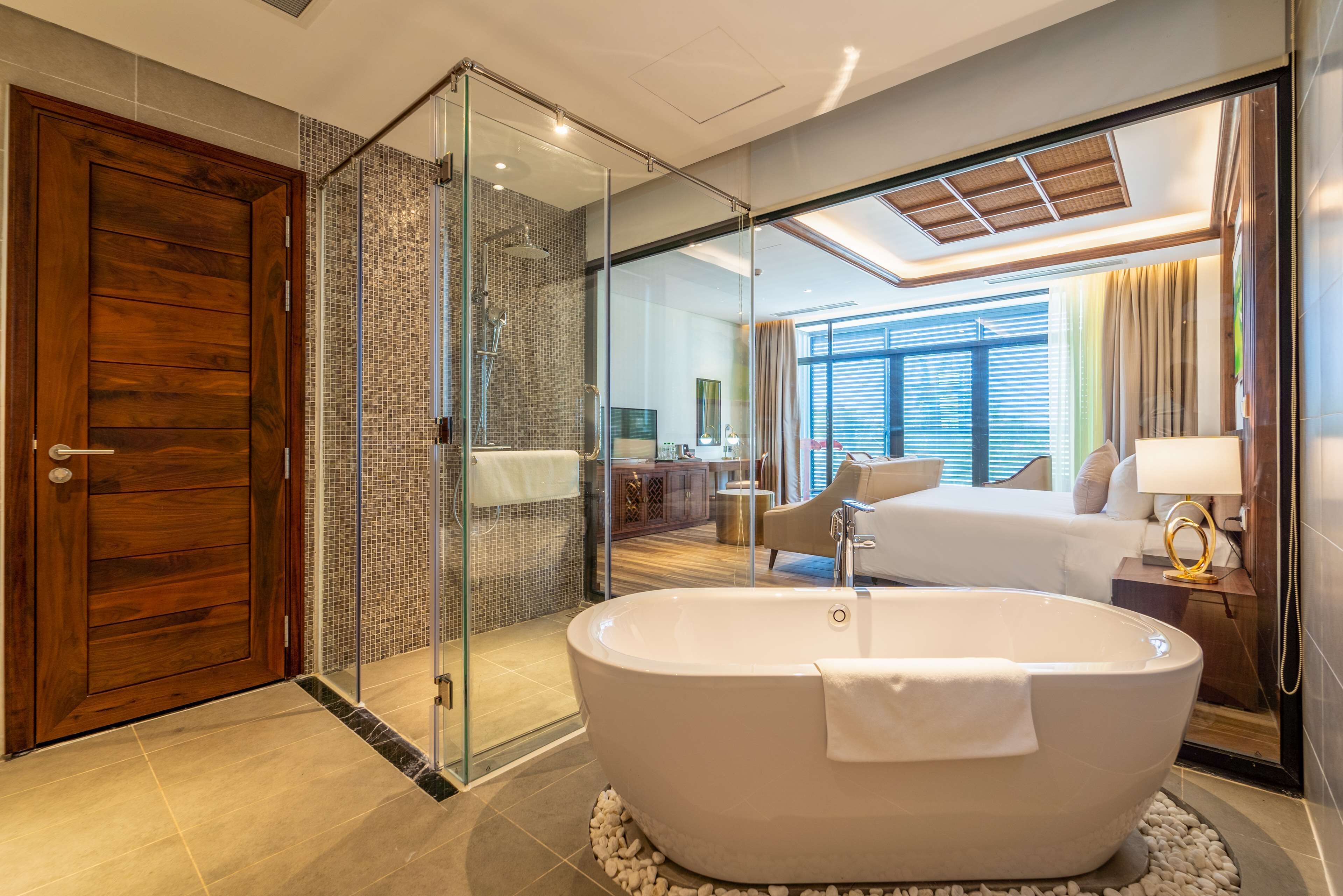 Een moderne badkamer met een vrijstaand bad, een douche met glazen wanden en een houten deur.