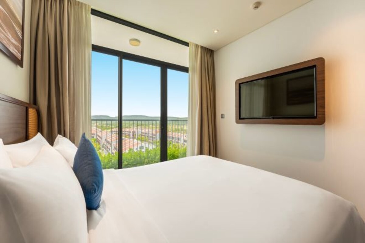 Une chambre d’hôtel dotée d’un grand lit, d’un téléviseur à écran plat fixé au mur et offrant une vue sur le paysage urbain par une grande fenêtre.