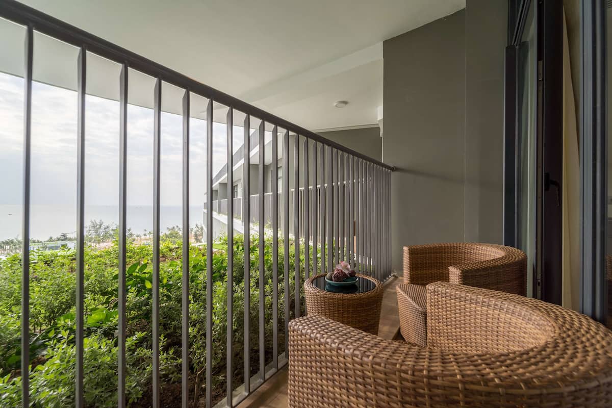 Ein Balkon mit Korbmöbeln, einem Geländer und Blick auf Grünflächen und eine entfernte Landschaft.