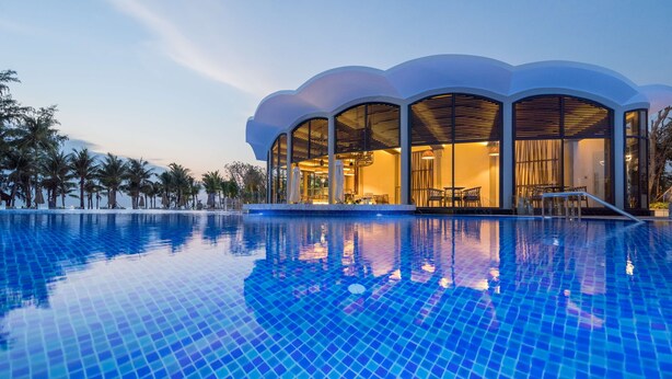 Un hôtel moderne doté d’une grande piscine, de larges fenêtres et situé dans un cadre tropical.