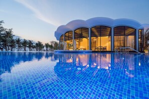 Ein modernes Hotel mit großem Swimmingpool, großen Fenstern und tropischer Umgebung.