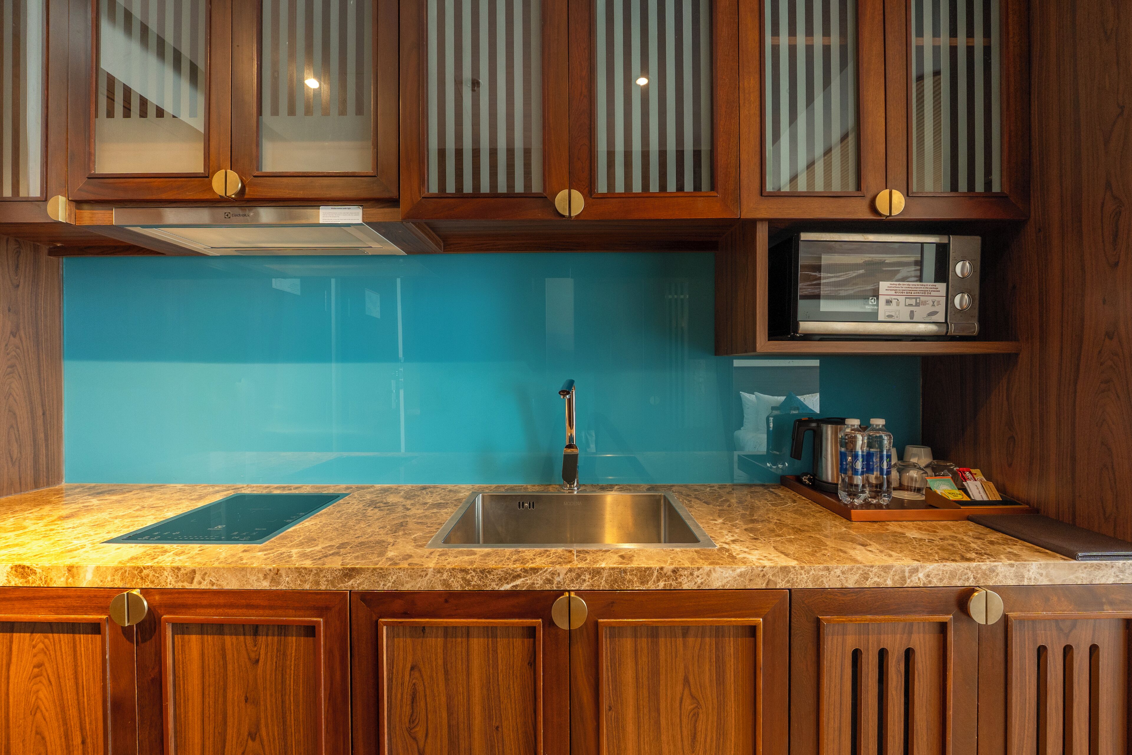 A kitchen with wooden cabinets, a stainless steel sink, a microwave, and a blue backsplash.