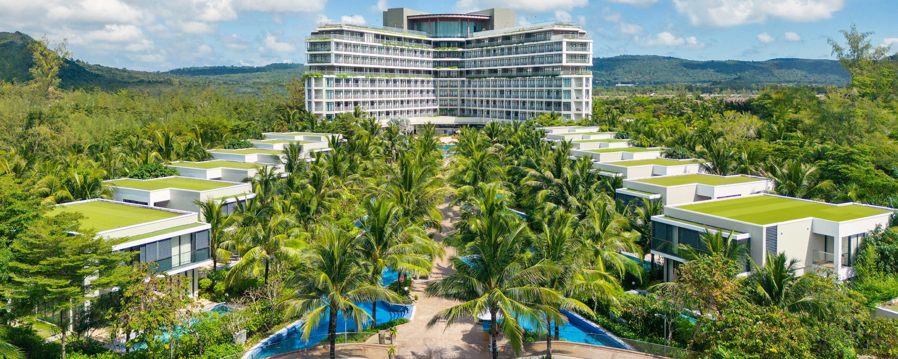 A modern hotel with a rooftop pool, surrounded by lush greenery and palm trees.