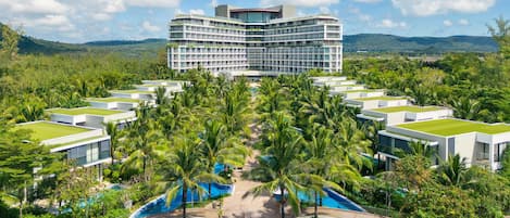 A modern hotel with a rooftop pool, surrounded by lush greenery and palm trees.