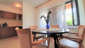 A dining area with a round table, four chairs, a vase with a plant, and a window with curtains. - Apartment Cherry with spacious terrace & Wi-Fi (Krk)