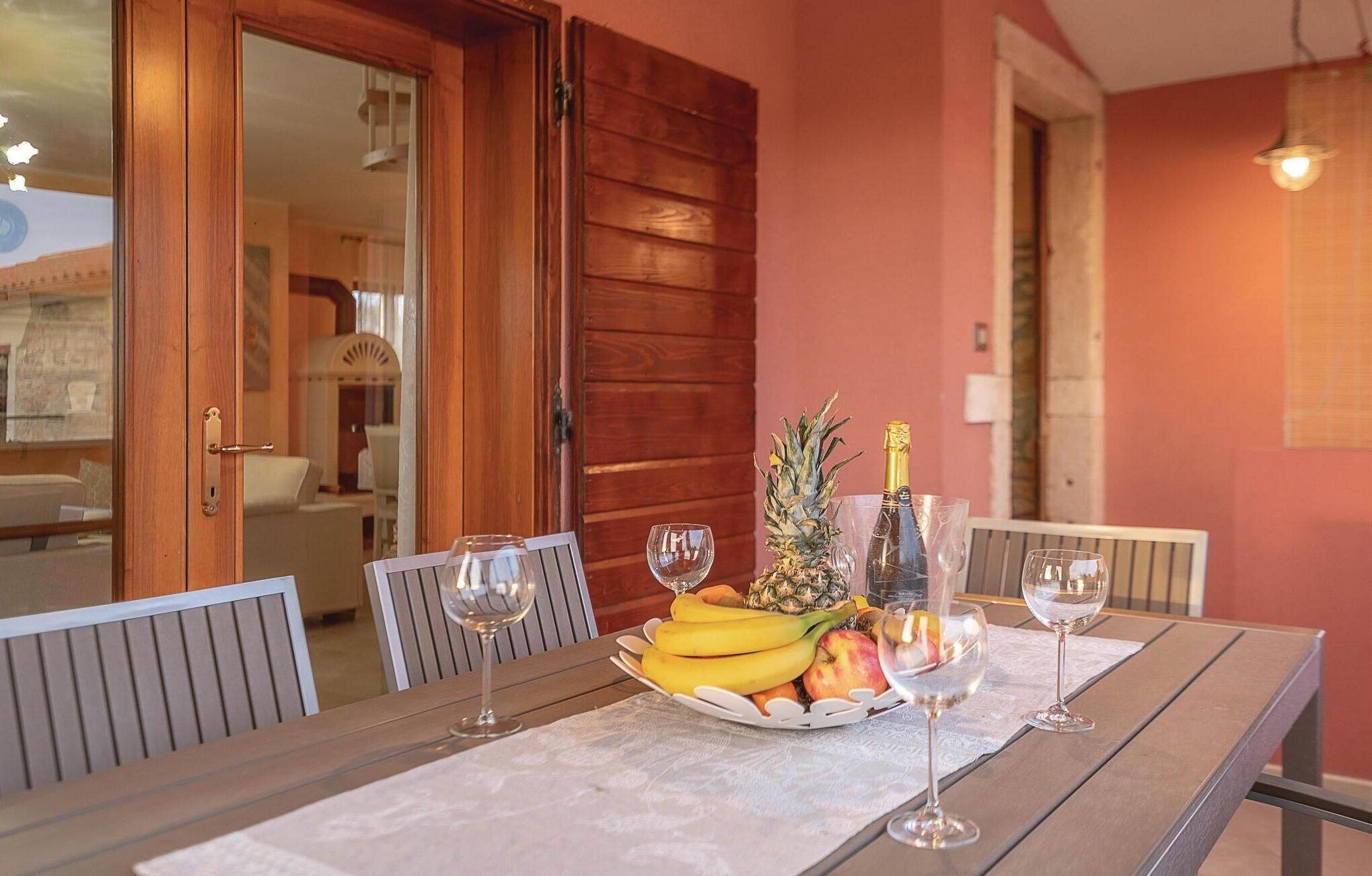 A dining table with a fruit basket, wine glasses, and a bottle of champagne.