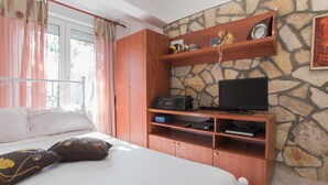 A bedroom with a bed, a wooden TV stand with a television, and a stone wall. - Apartments Ana (Vodice)