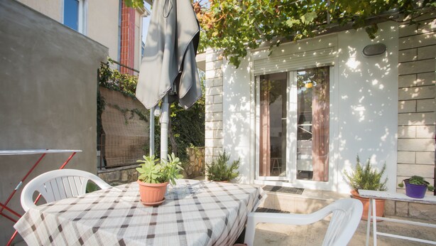 A patio with a table and chairs, a potted plant, and a building entrance. - Apartments Ana (Vodice)