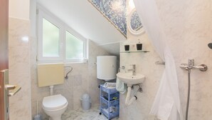 A bathroom with a toilet, sink, and shower. There is a window above the toilet and a towel rack above the sink. - Apartments Ana (Vodice)