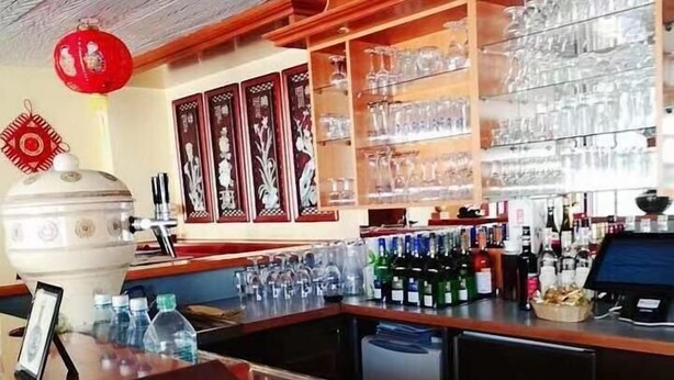 A bar area with a wooden ceiling, shelves with glasses, bottles, and a menu stand. - Hotel Quellenhof (Bad Breisig)