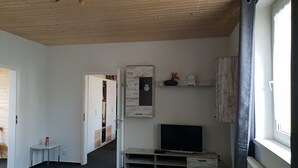 A room with a wooden ceiling, a television on a wooden stand, a mirror, and a shelf with decorative items.
