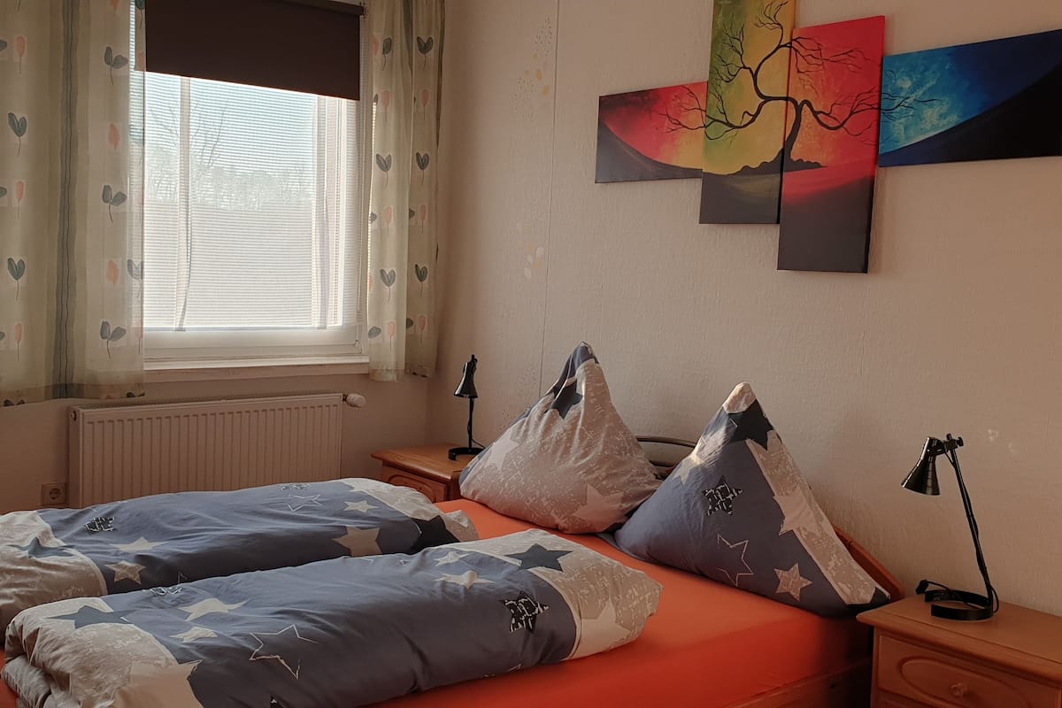 A bedroom with a bed, two bedside tables, a nightstand, and a window with curtains.