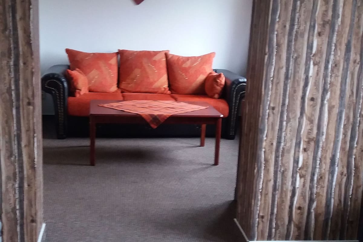A room with a sofa, a wooden table, and a patterned bedspread.