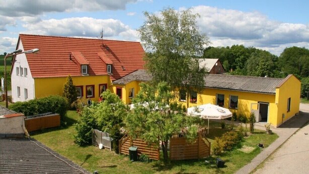 A yellow building with a red roof, surrounded by greenery and a small tree.