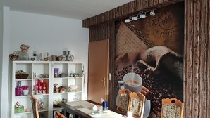 A cozy room with a wooden wall, a white shelf with various items, and a large coffee-themed mural.