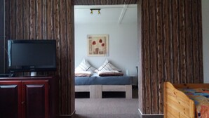 A room with a wooden wall, a bed with pillows, a television on a stand, and a painting on the wall.