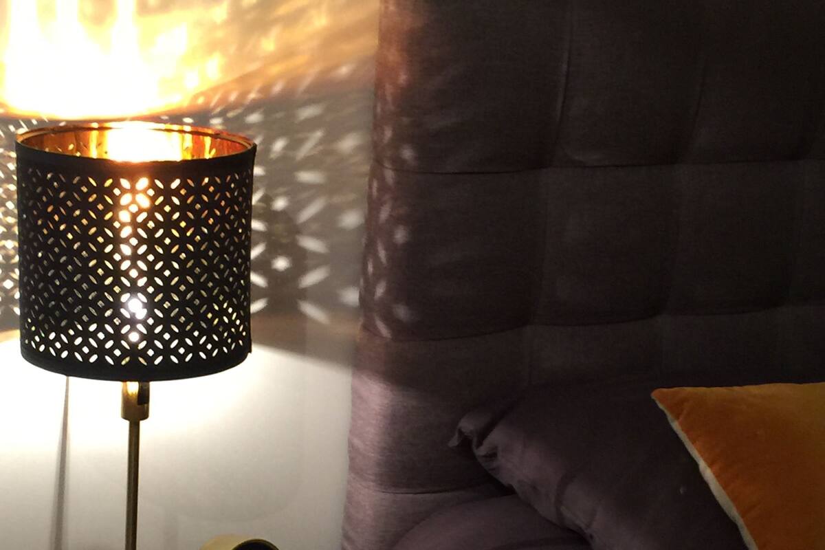 Un comodino con una lampada, uno specchio piccolo e un mobiletto in legno.
