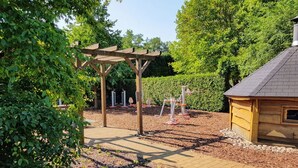 Een tuin met een houten pergola, een kleine schuur en een haag.