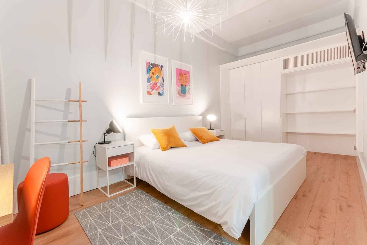Ein Schlafzimmer mit Bett, Nachttischen, einem Sessel, einem Schreibtisch und einem Kleiderschrank.