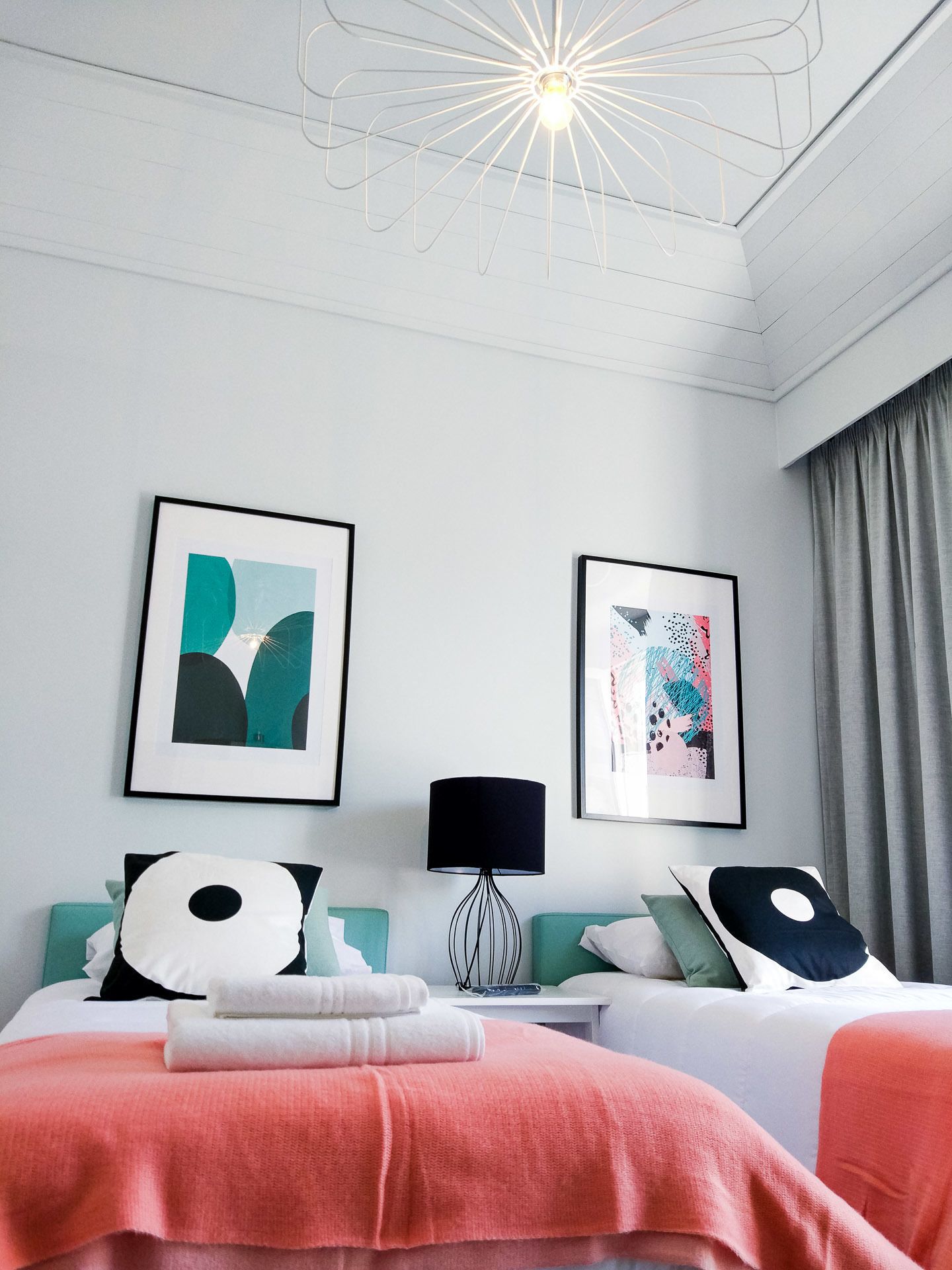 Una habitación de hotel moderna con una cama, dos cuadros enmarcados, una lámpara y un aplique de techo original.