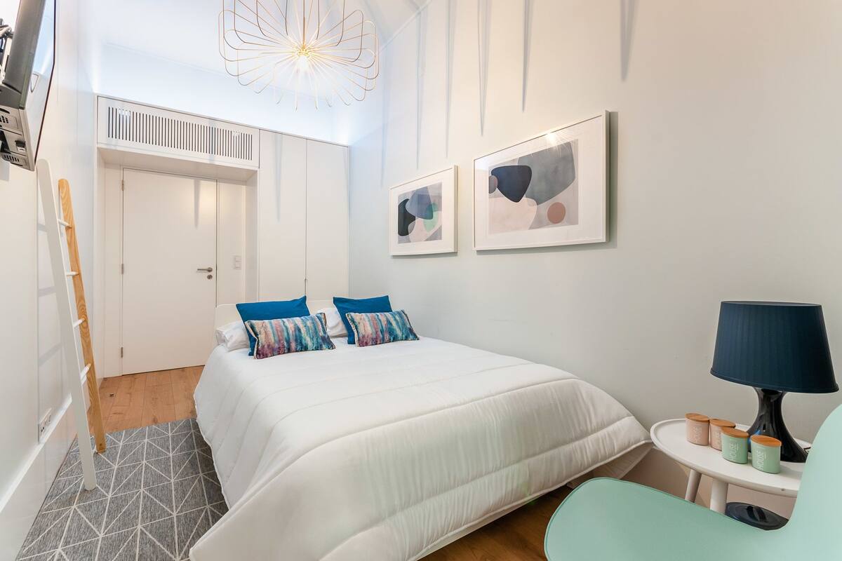 Ein Schlafzimmer mit einem Bett, einem Schreibtisch, einem Stuhl, einer Lampe und zwei abstrakten Bildern an der Wand.