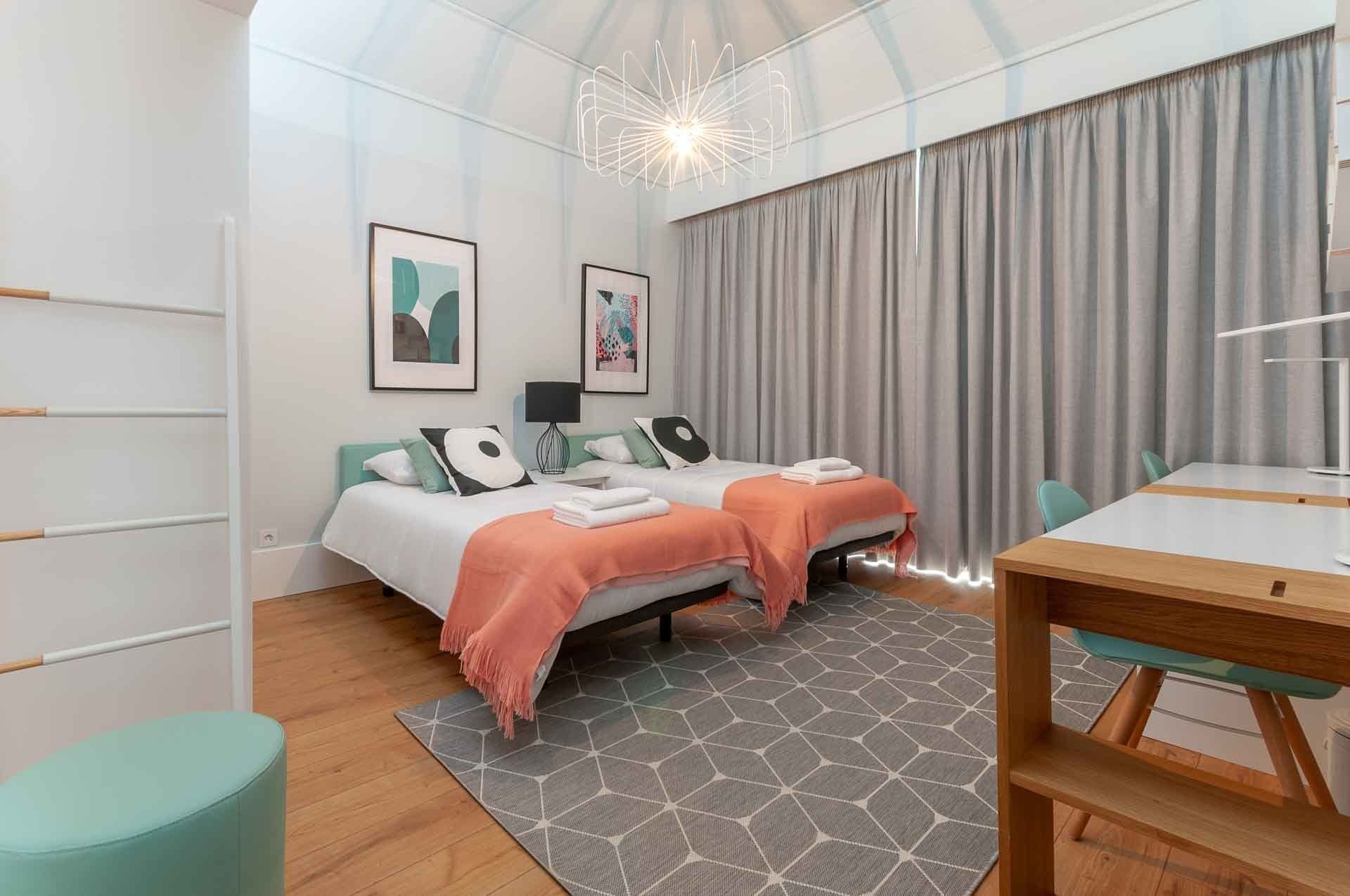 Una habitación de hotel moderna con dos camas, una mesa de comedor y un amplio ventanal con cortinas.