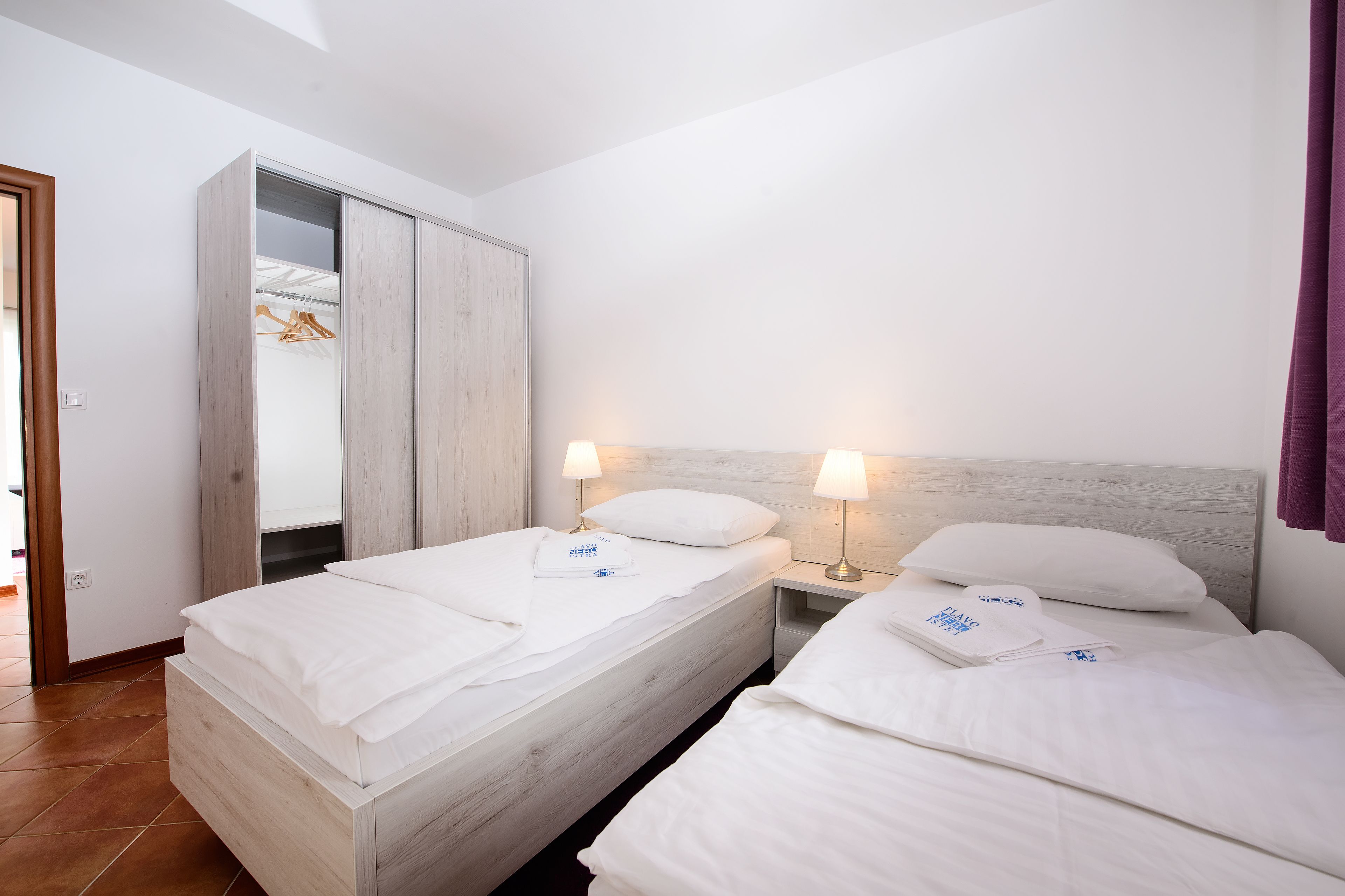 A hotel room with two beds, a wardrobe, and bedside lamps.