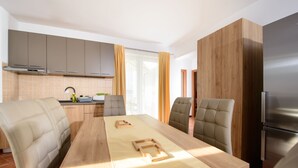 A modern kitchen with a dining area, featuring a long wooden table, cushioned chairs, and a built-in oven. - Plavo Nebo Istra Apartments (Medulin)