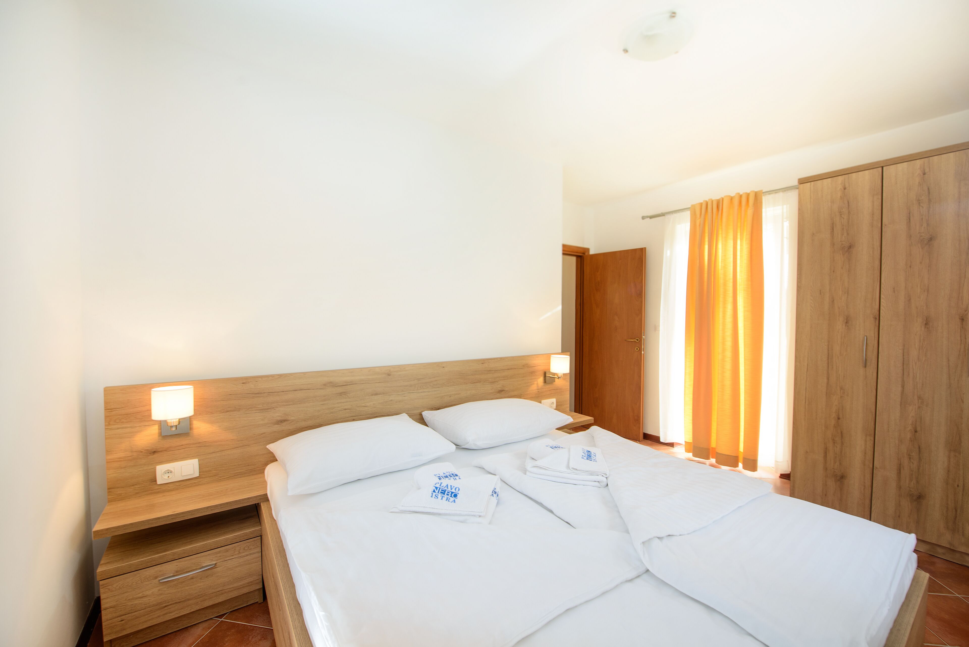 Un lit bien fait, avec du linge de lit blanc, une tête de lit en bois et une table de chevet avec une lampe.