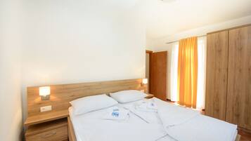 A neatly made bed with white linens, a wooden headboard, and a nightstand with a lamp.