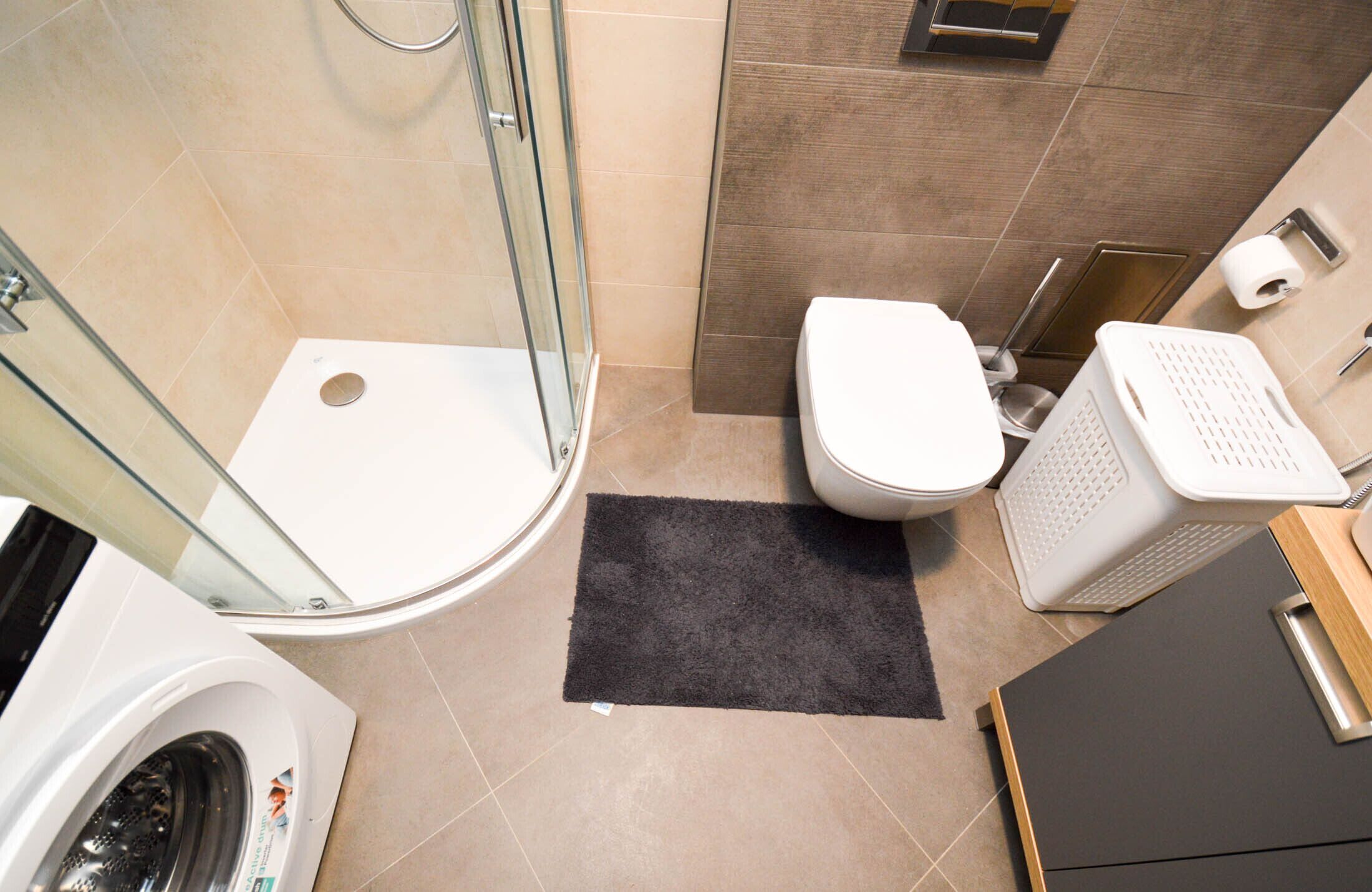 Een kleine badkamer met een douchecabine van glas, toilet, wasmachine en een klein wasmandje.