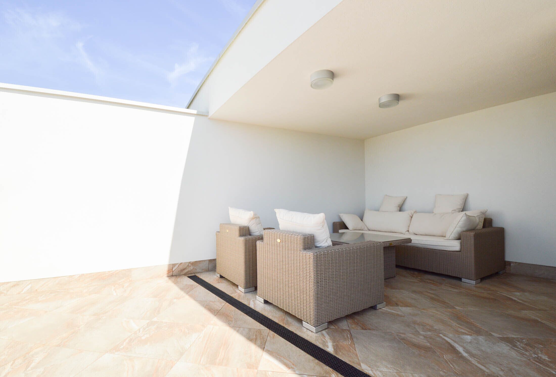 Un espace extérieur ensoleillé, aménagé avec un canapé et des fauteuils en osier, une petite table et une vue sur le ciel.
