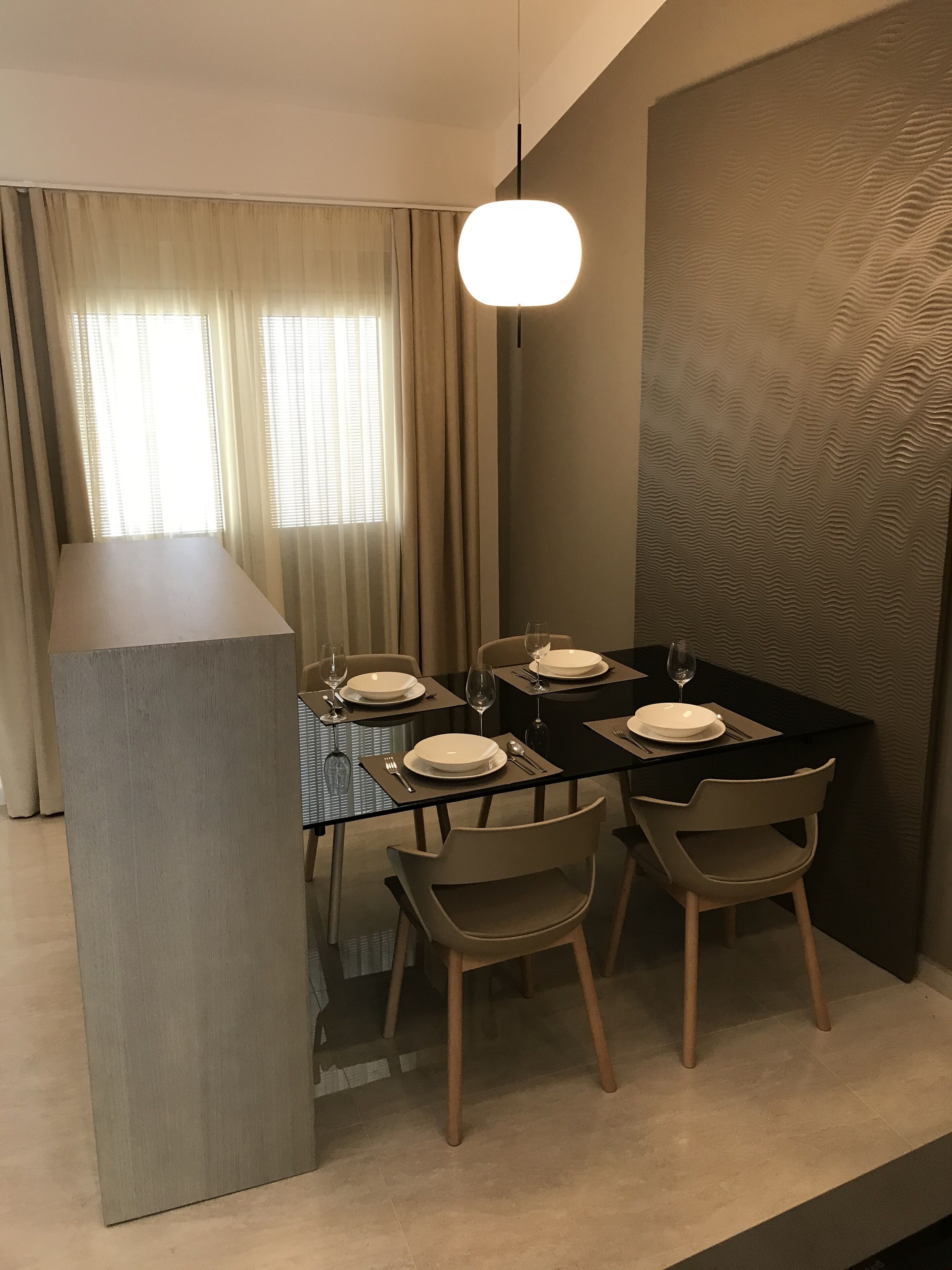 Een eetgedeelte met een glazen tafel, vier stoelen en een moderne hanglamp.