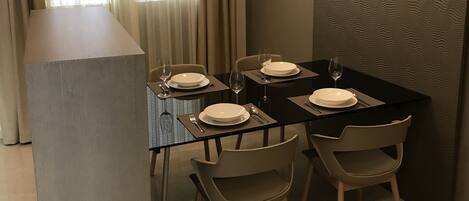 A dining area with a glass table, four chairs, and a modern pendant light.