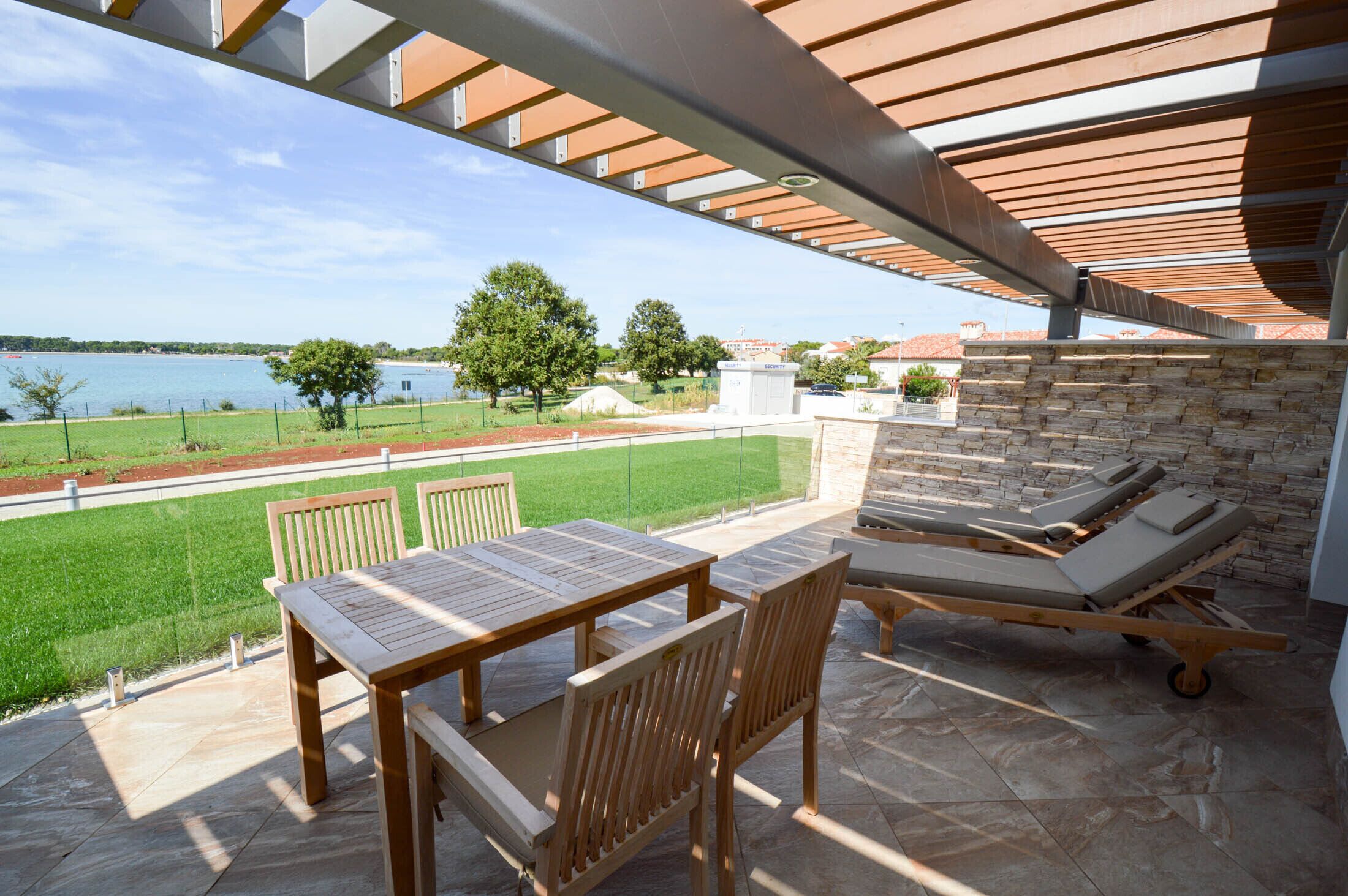 Eine Außenpatio mit Tisch und Stühlen, eine Lounge-Ecke mit Kissen und Blick auf einen See und viel Grün.