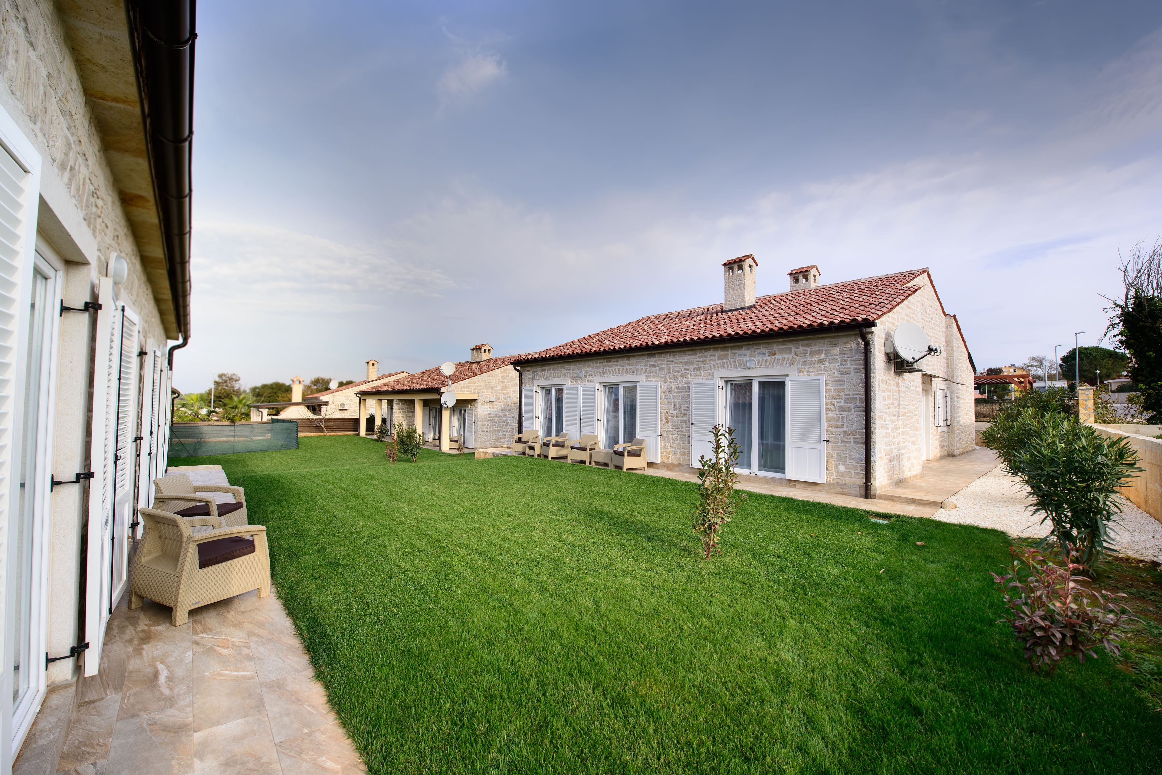 A property with a well-maintained lawn, a patio with outdoor seating, and a stone building with a tiled roof.