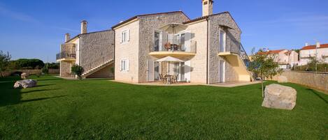 A two-story stone house with a balcony, a staircase, and a well-maintained lawn.
