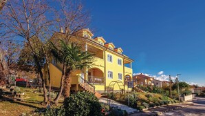A yellow building with a balcony, surrounded by greenery and a clear sky. - Stunning apartment in Kostrena with WiFi (Kostrena)