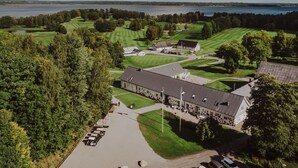 A golf course with a clubhouse, parking area, and a lake in the background. - Skyrup Golf & Hotell (Tyringe)