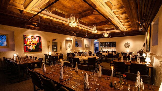 A restaurant with wooden tables set for dining, chandeliers, and a large painting on the wall. - Skyrup Golf & Hotell (Tyringe)