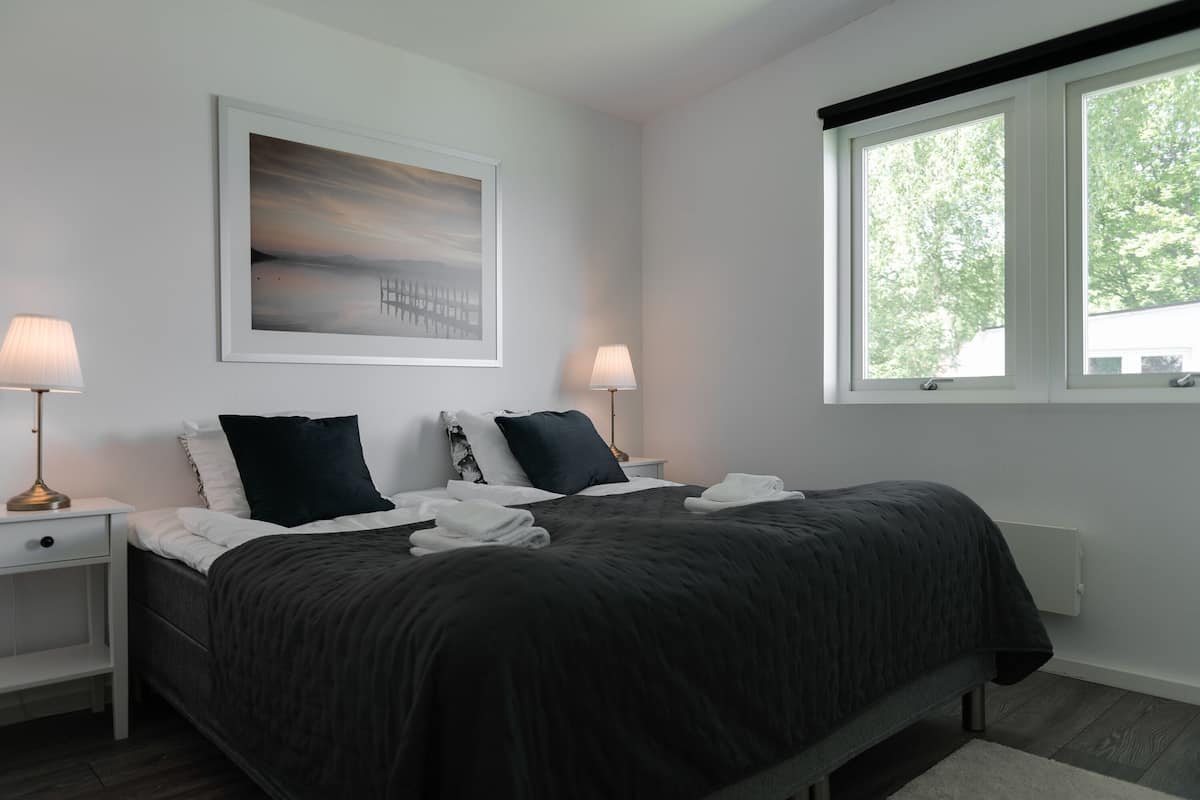Um quarto com uma cama, duas mesas de cabeceira, luminárias, um quadro e uma janela.