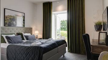 A bedroom with a bed, a nightstand, a chair, a table with a plant, and a window with curtains.