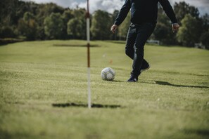 Una persona jugando al fútbol en un campo cubierto de hierba, con árboles al fondo.