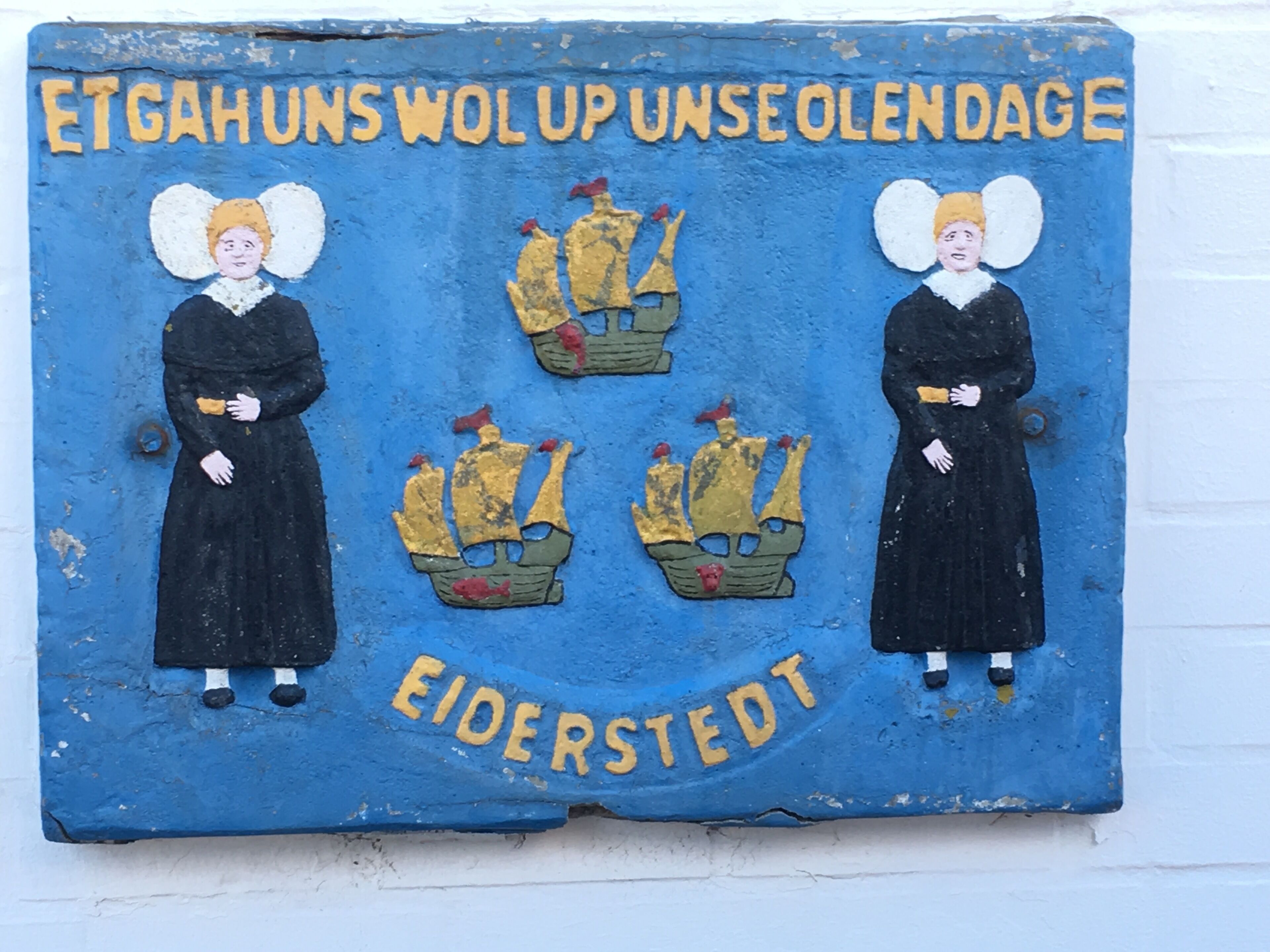 A blue sign with two figures and ships, labeled "ETGAHUNS WOL UP UNSEOLENDAGE" and "EIDERSTEDT".