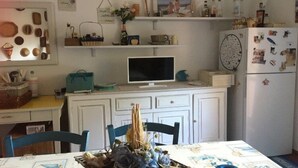 A kitchen with white cabinets, a dining table with a blue tablecloth, and a refrigerator with magnets. - A Pochi Passi dal Mare di Marciana Marina (Marciana Marina)